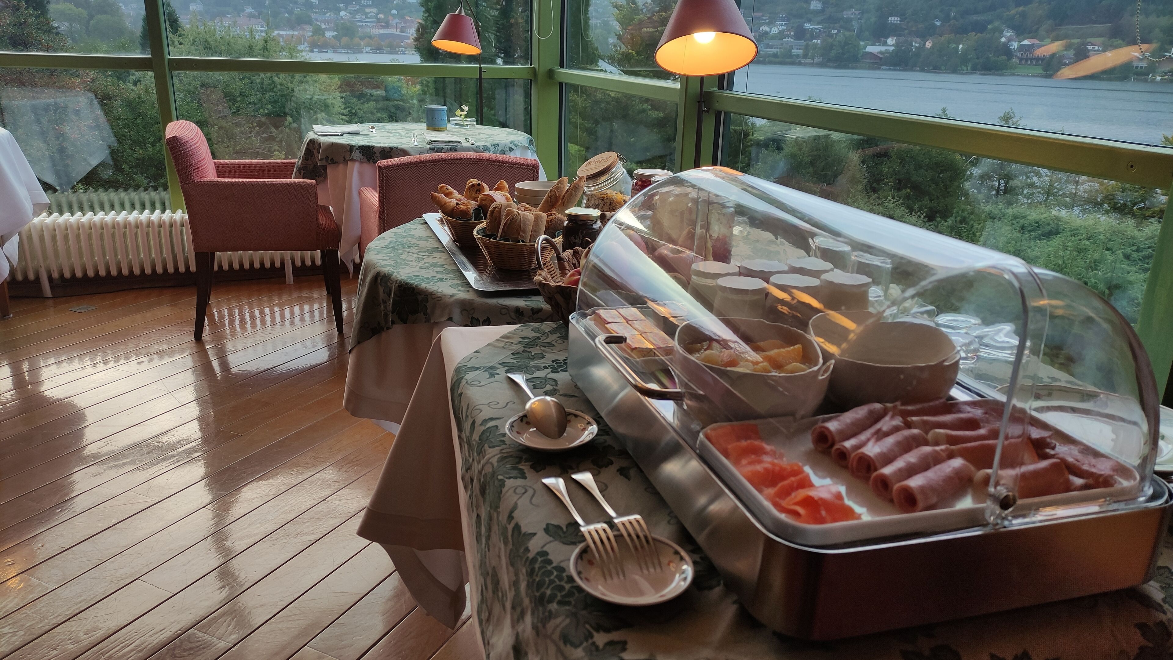 Un bufé de desayuno con diversas opciones de comida y vista a un lago a través de amplias ventanas.