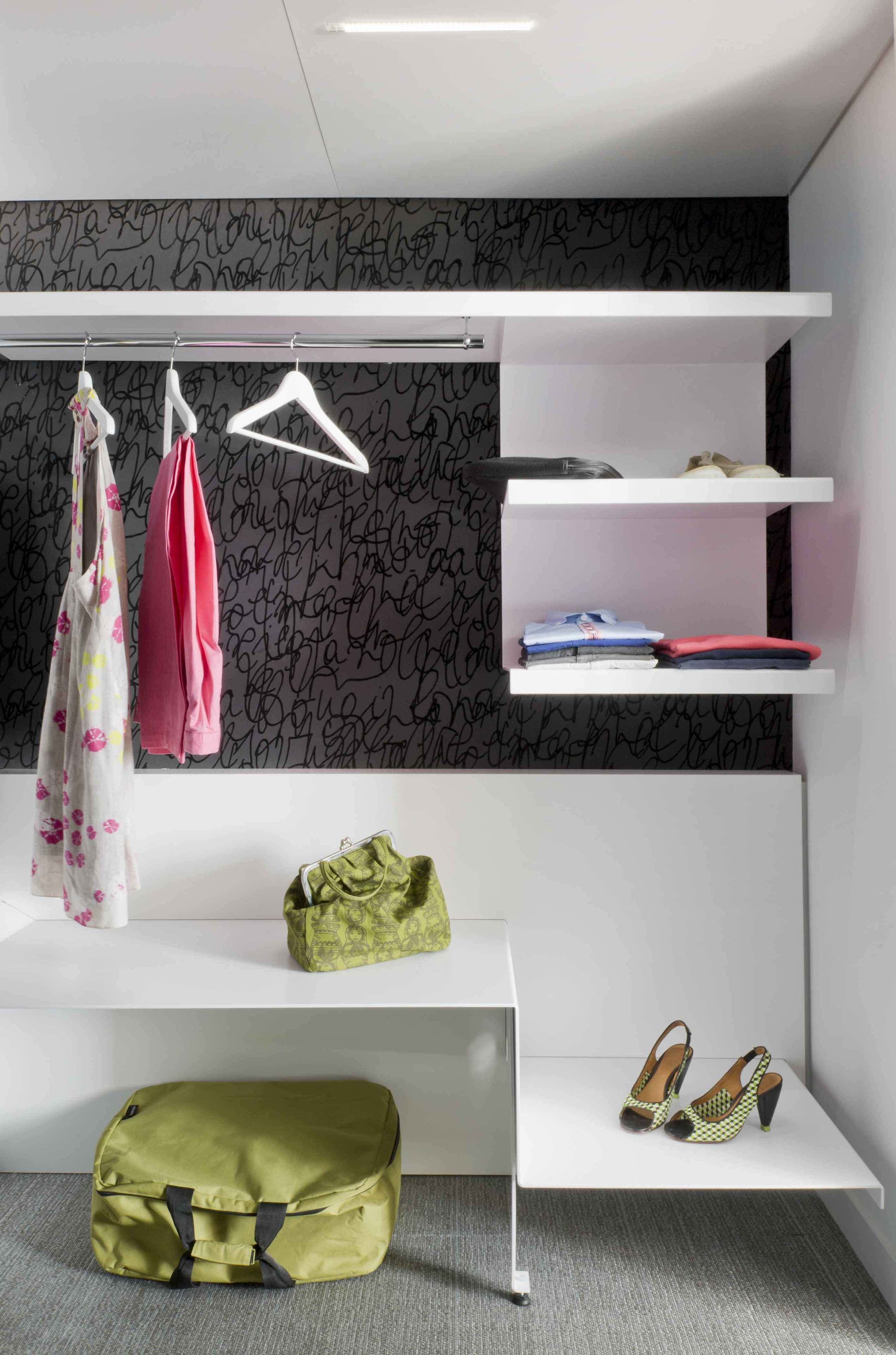 Een moderne kamer met een witte bank, een groene tas, schoenen en kleding aan een rek.