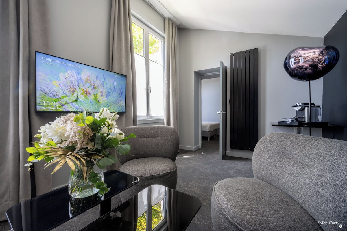 A modern living room with a flat-screen TV, a vase with flowers, a grey sofa, and a unique spherical lamp.