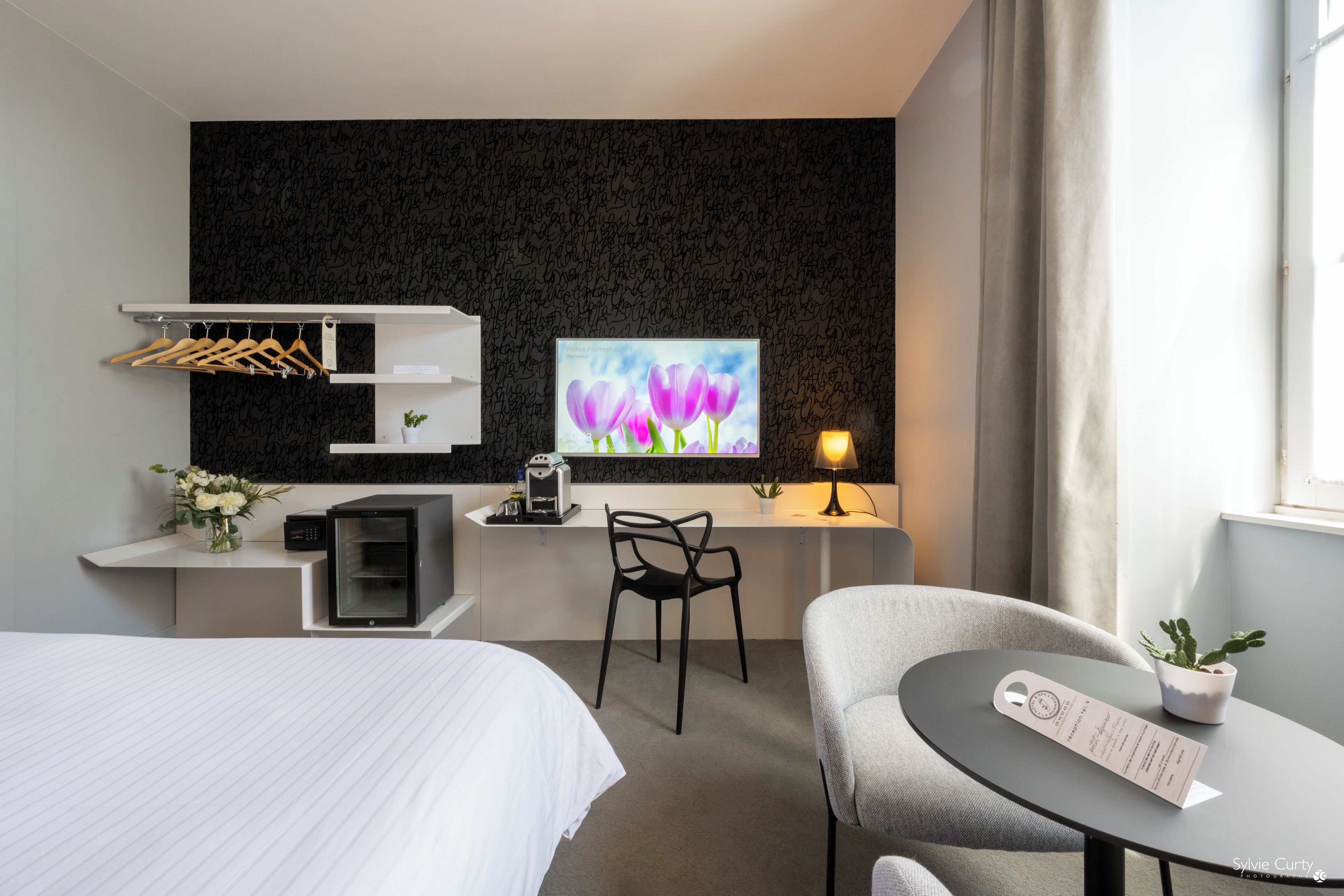 Habitación de hotel con cama, escritorio con computadora, silla, una mesita con un menú y televisor montado en la pared.