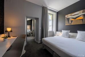 Enjoy a comfortable stay in this stylish room with a large bed, desk, and seating area, offering a view of the outside through a window.