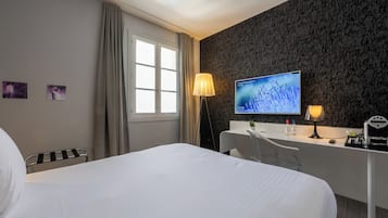 A hotel room with a bed, a desk with a computer, a lamp, and a TV displaying a nature scene.
