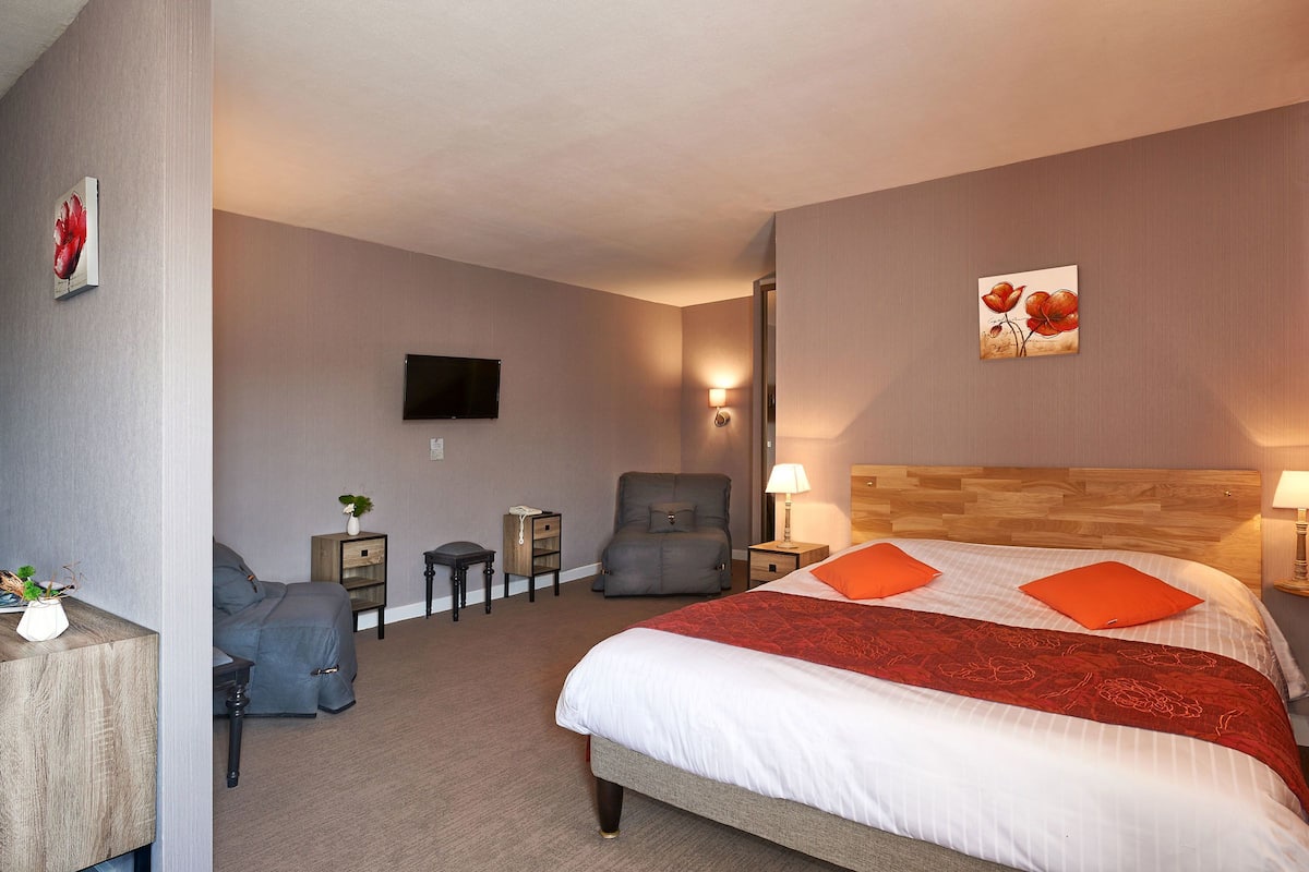 A hotel room with a large bed, a desk with a chair, a TV, and a chair.