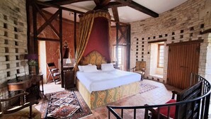 Un dormitorio con una cama grande, una silla de madera, una mesita y una ventana.