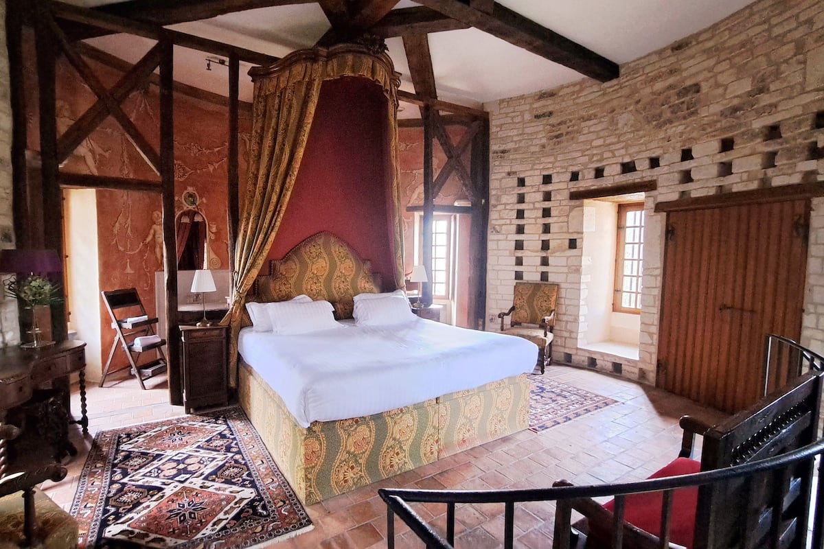 Une chambre avec un grand lit, une chaise en bois, une petite table et une fenêtre.