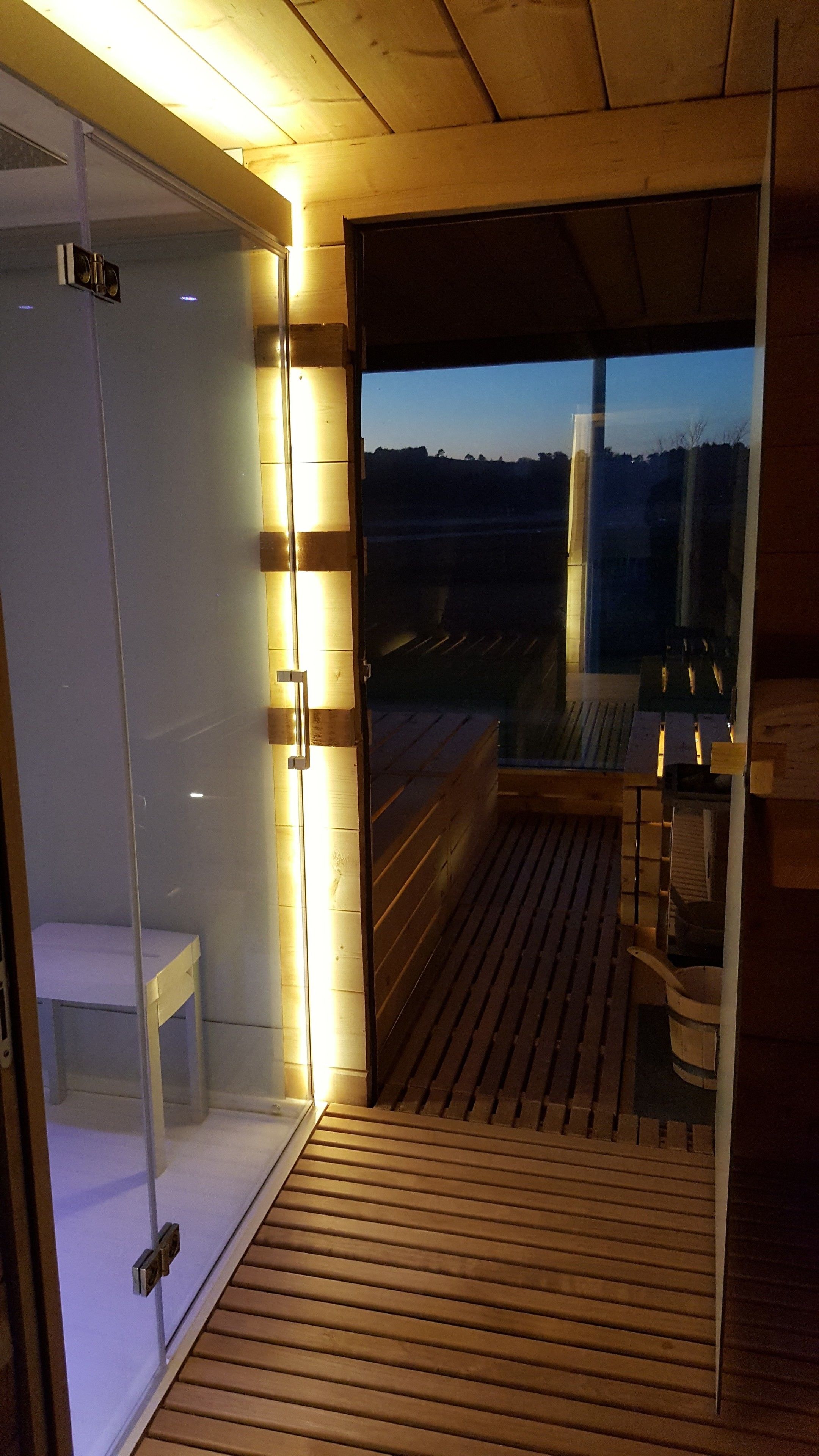 A wooden deck with a glass enclosure, a white bench, and a wooden table with a bucket.