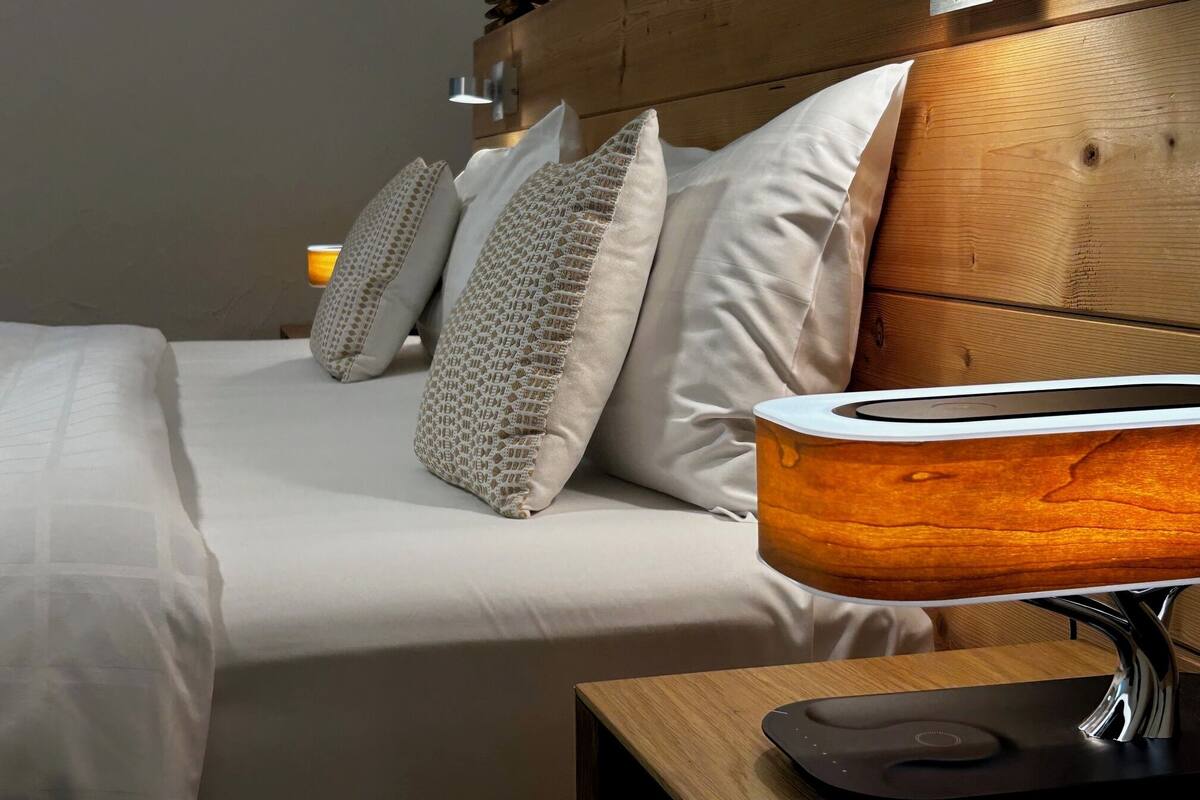 A neatly made bed with a wooden headboard, a bedside table with a modern lamp, and a wall-mounted light fixture.