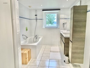 A modern bathroom with a bathtub, shower, and sink. - Hôtel Sports & Spa La Voile d'Or (Plurien)