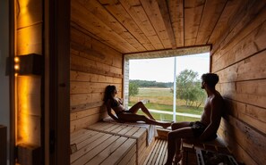 A wooden cabin with a large window offering a view of a grassy field. - Hôtel Sports & Spa La Voile d'Or (Plurien)