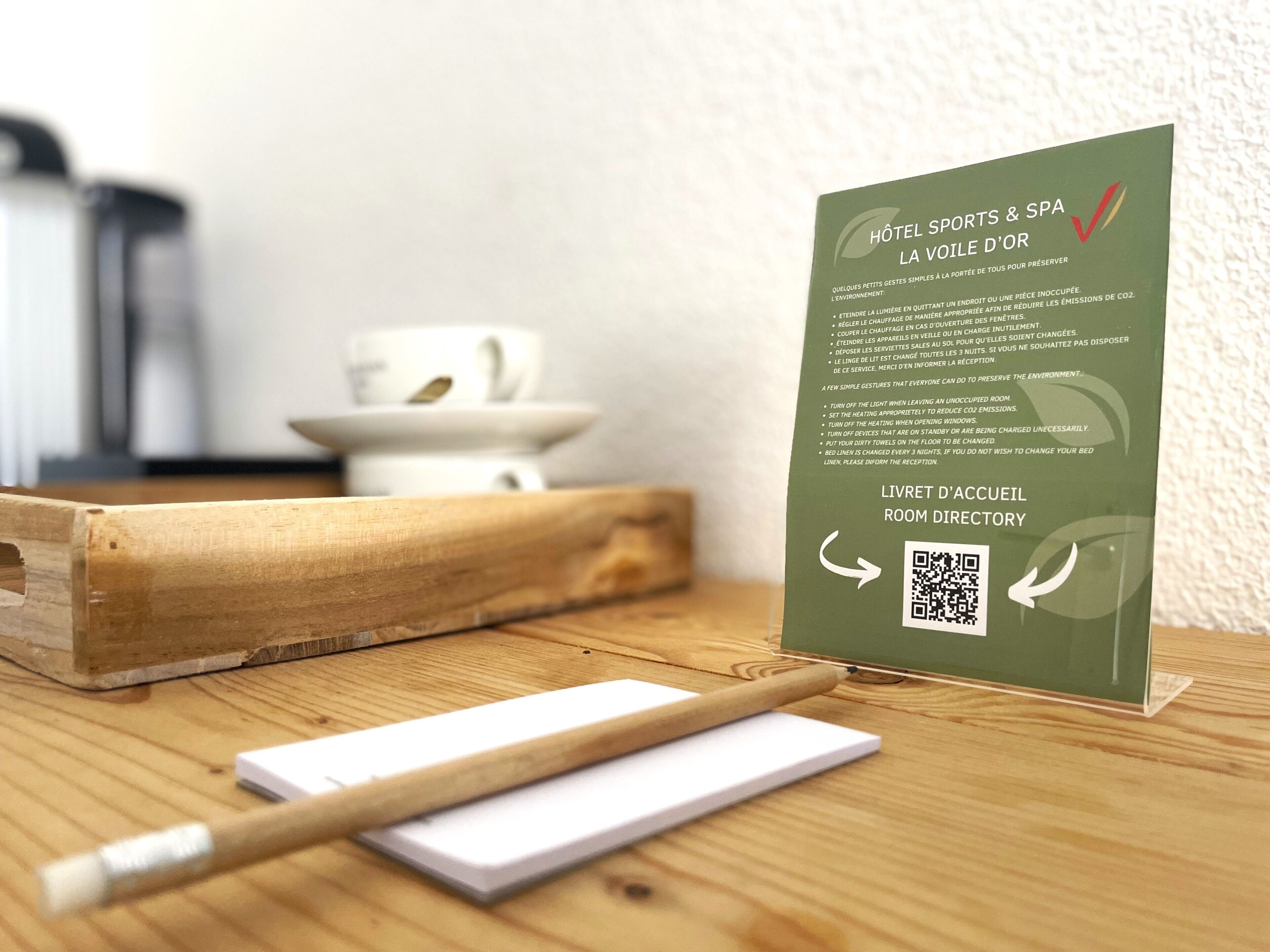 Balcão de recepção de hotel com uma placa informativa verde, uma caixa de madeira e um bloco de notas branco.
