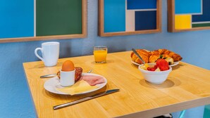 A breakfast table with croissants, a bowl of fruit, a cup, and a plate with eggs and ham. - ibis Styles Lyon Croix Rousse (Lyon)