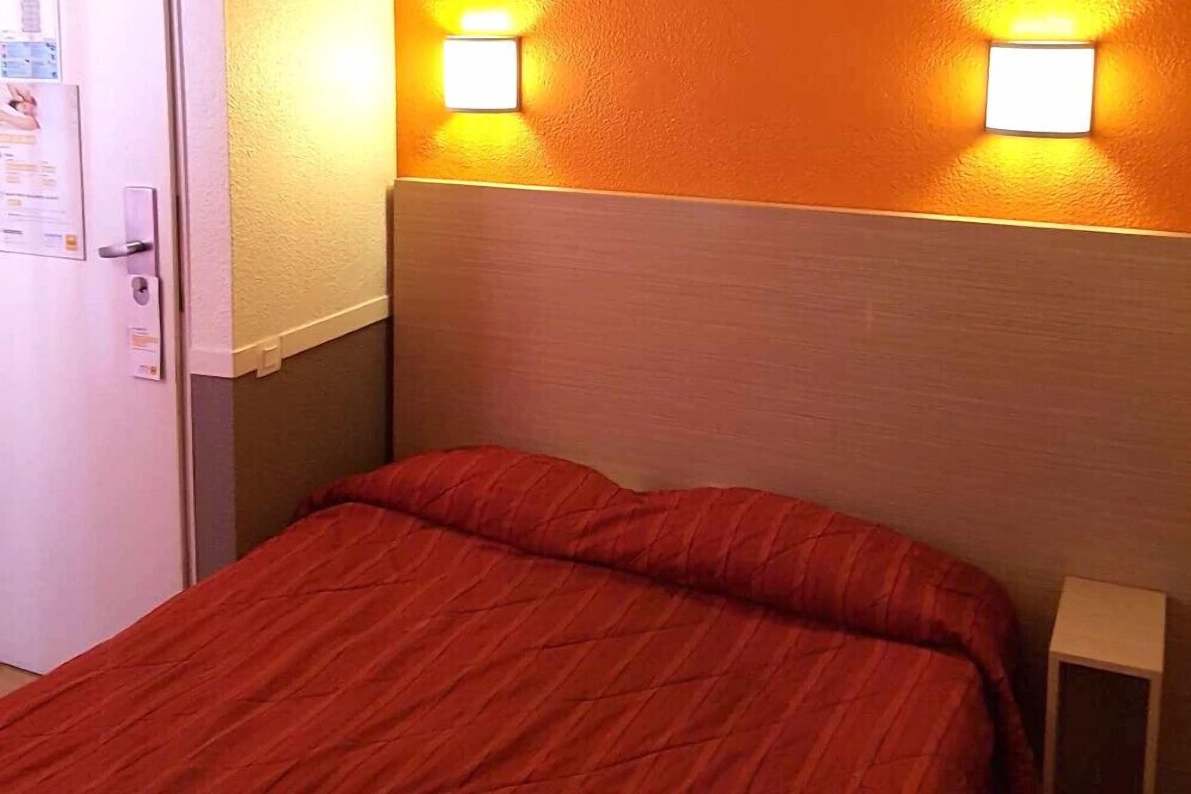 Une chambre d’hôtel avec un lit, deux lampes fixées au mur et une porte dotée d’une serrure.