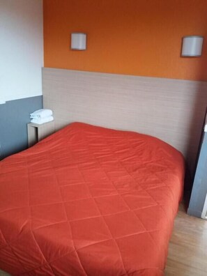 A hotel room with a large bed, a nightstand with a phone and a towel, and two wall-mounted lamps. - HECO Colmar Nord - ex Première Classe (Houssen)