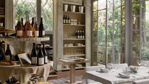 A dining area with a table set for two, a wine rack with bottles, and a view of greenery through large windows. - L'Hôtel Particulier (Arles)