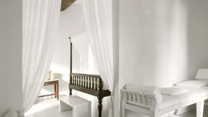 A room with a white bed, a wooden bench, a small table, and a wall-mounted lamp. - L'Hôtel Particulier (Arles)