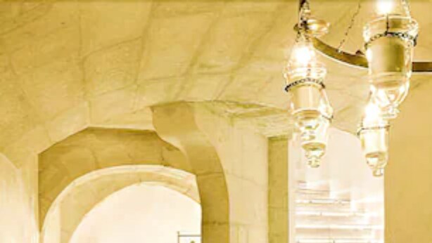 A hallway with a staircase, stone walls, and a chandelier. - L'Hôtel Particulier (Arles)