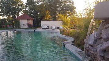 A swimming pool with a waterfall feature, surrounded by a stone wall and greenery.