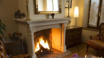 Una sala de estar acogedora con chimenea, sillones de cuero, una mesa de centro con fruta y velas, y un espejo grande sobre la repisa.