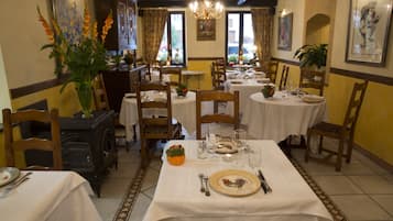 A dining area with multiple tables set for meals, wooden chairs, and a vintage stove.