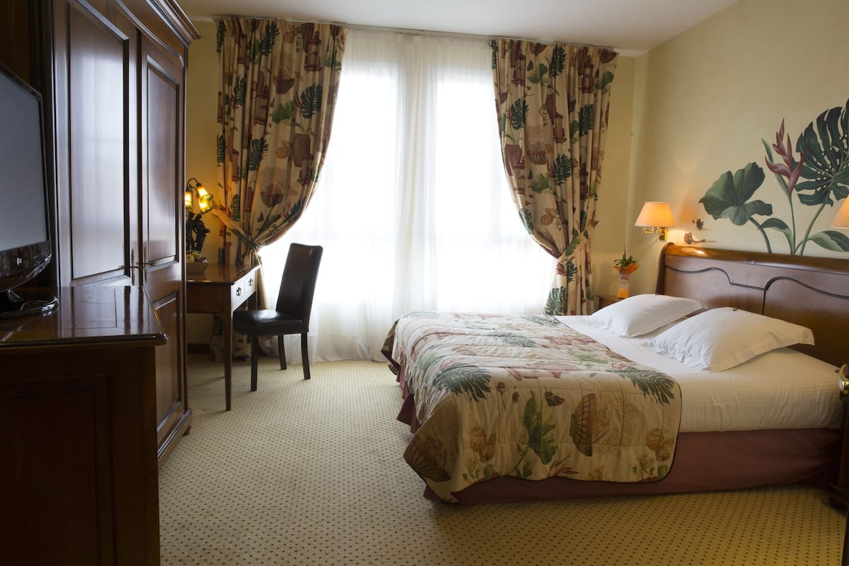 Une chambre d’hôtel avec un lit, un bureau, une chaise, une télévision et des rideaux.