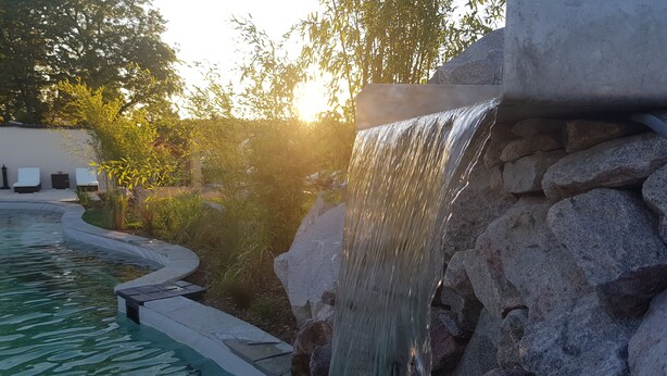 Een waterval in een zwembadgedeelte met helder water, omringd door rotsen en begroeiing.