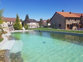 Una piscina cristalina con borde de piedra, rodeada de casas con techos de tejas rojas y muros de piedra.