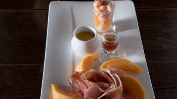 Un plato rectangular blanco con melón en rodajas, jamón serrano y dos pequeños vasos de salsa sobre una mesa de madera.