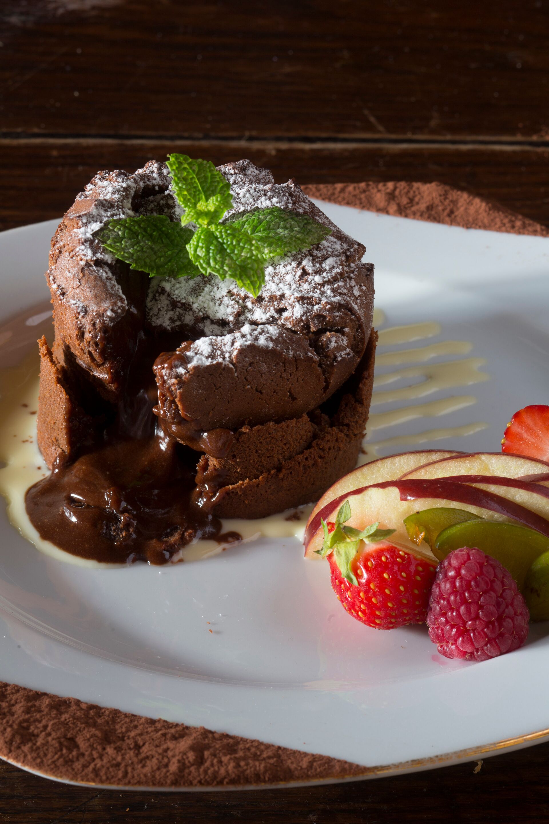 A dessert with chocolate lava cake, mint leaves, and strawberries on a plate.