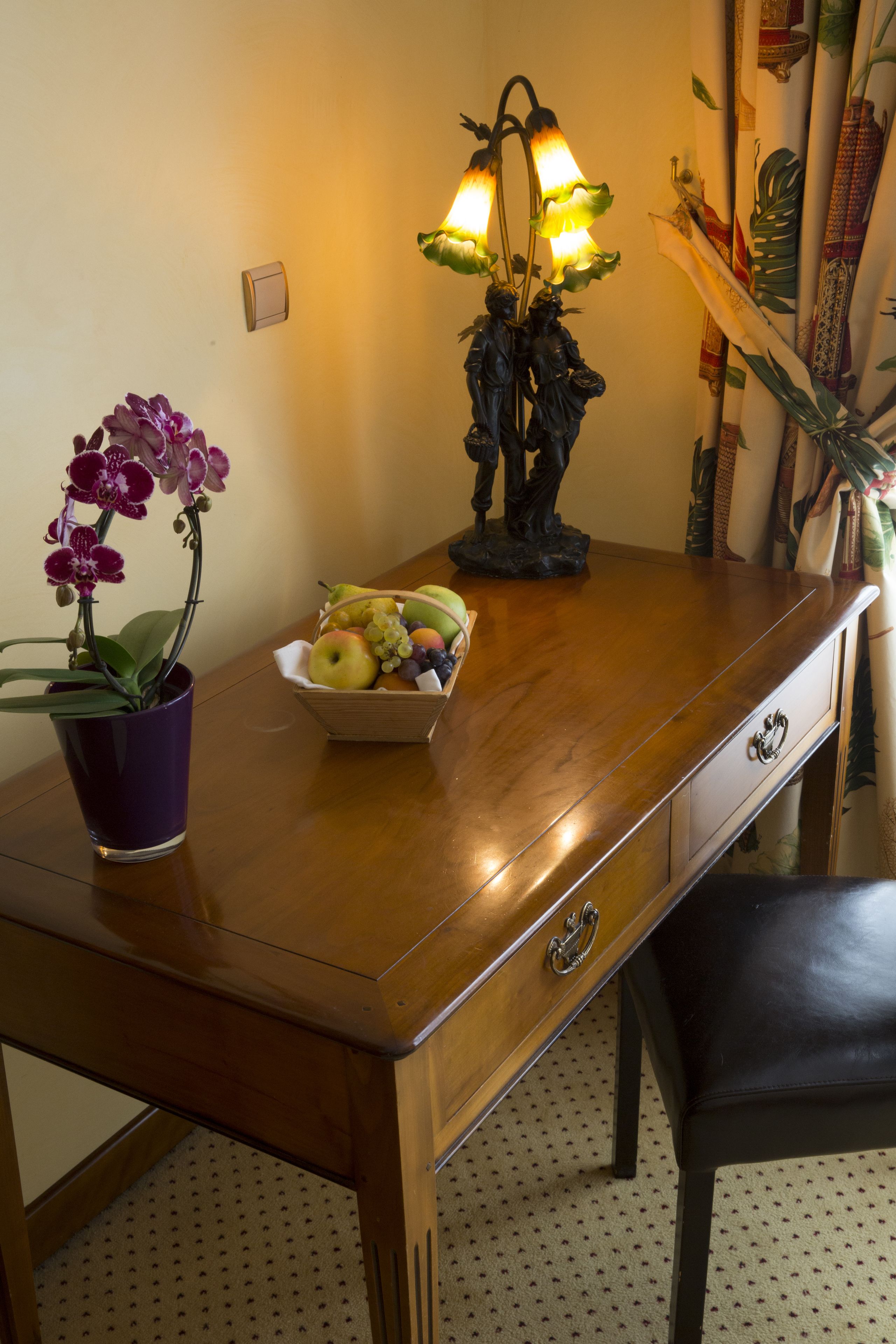 A wooden desk with a purple orchid pot, a fruit bowl, and a decorative lamp.