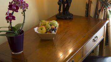 A wooden desk with a purple orchid pot, a fruit bowl, and a decorative lamp.