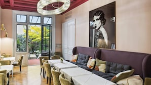 A dining area with a long table, cushioned seating, and a large painting on the wall. - Hôtel Le Paris Singulier (Paris)