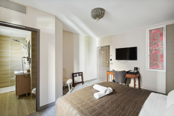 Une chambre d’hôtel comprenant un lit, un bureau, une chaise, une télévision et une salle de bain avec douche et toilettes.