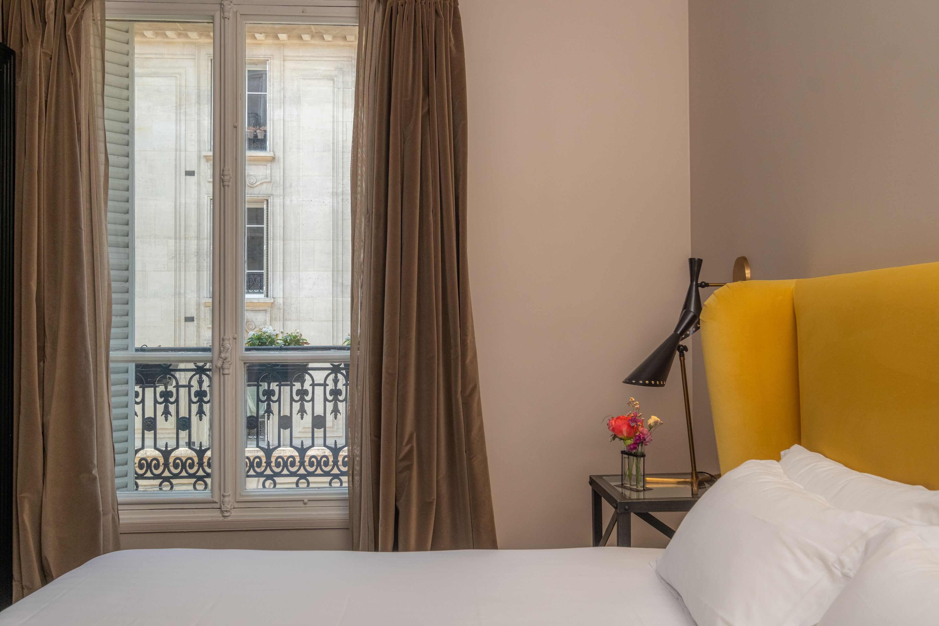 A hotel room with a bed, a nightstand with a lamp, and a window with curtains.
