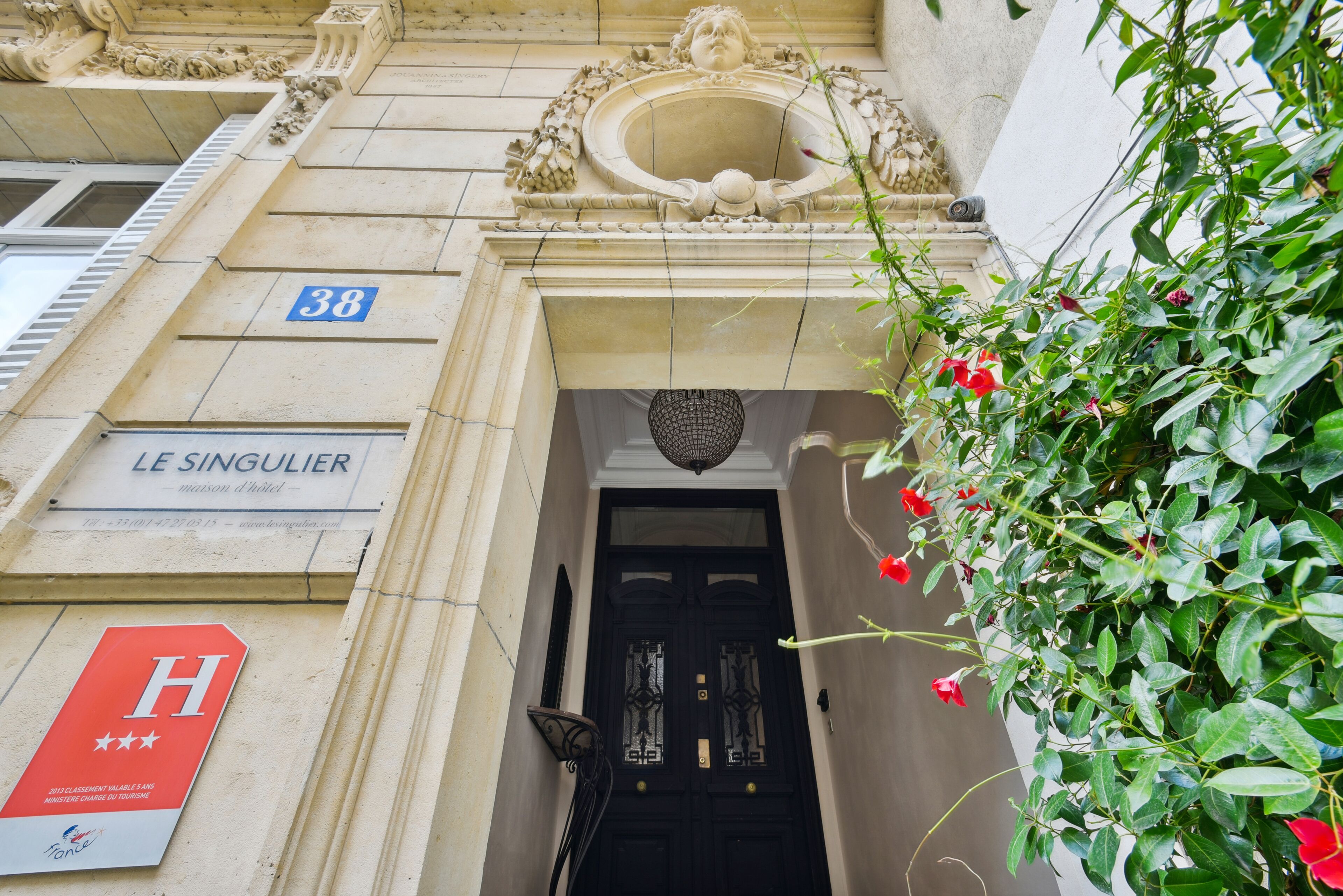 A building entrance with a black door, a sign reading "LE SINGULIER," and a blue number "38" sign.