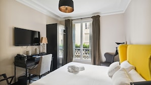 A hotel room with a bed, a desk with a computer, a television, and a window with curtains. - Hôtel Le Paris Singulier (Paris)