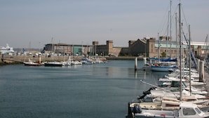 A marina with various boats docked, a building with a green roof, and a clear sky. - Citotel Beausejour (Cherbourg-en-Cotentin)