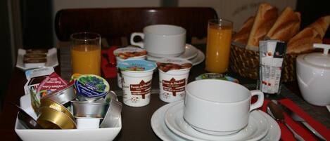 Une table de petit-déjeuner avec divers aliments, notamment du pain, du jus, ainsi que des pots de yaourt et des céréales.