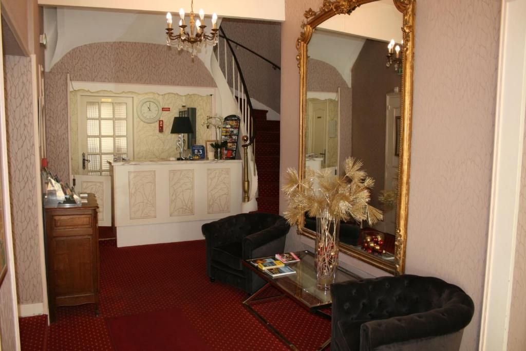 Une pièce avec une moquette rouge, un fauteuil noir, une table basse en verre, un miroir avec un cadre doré et un escalier en arrière-plan.