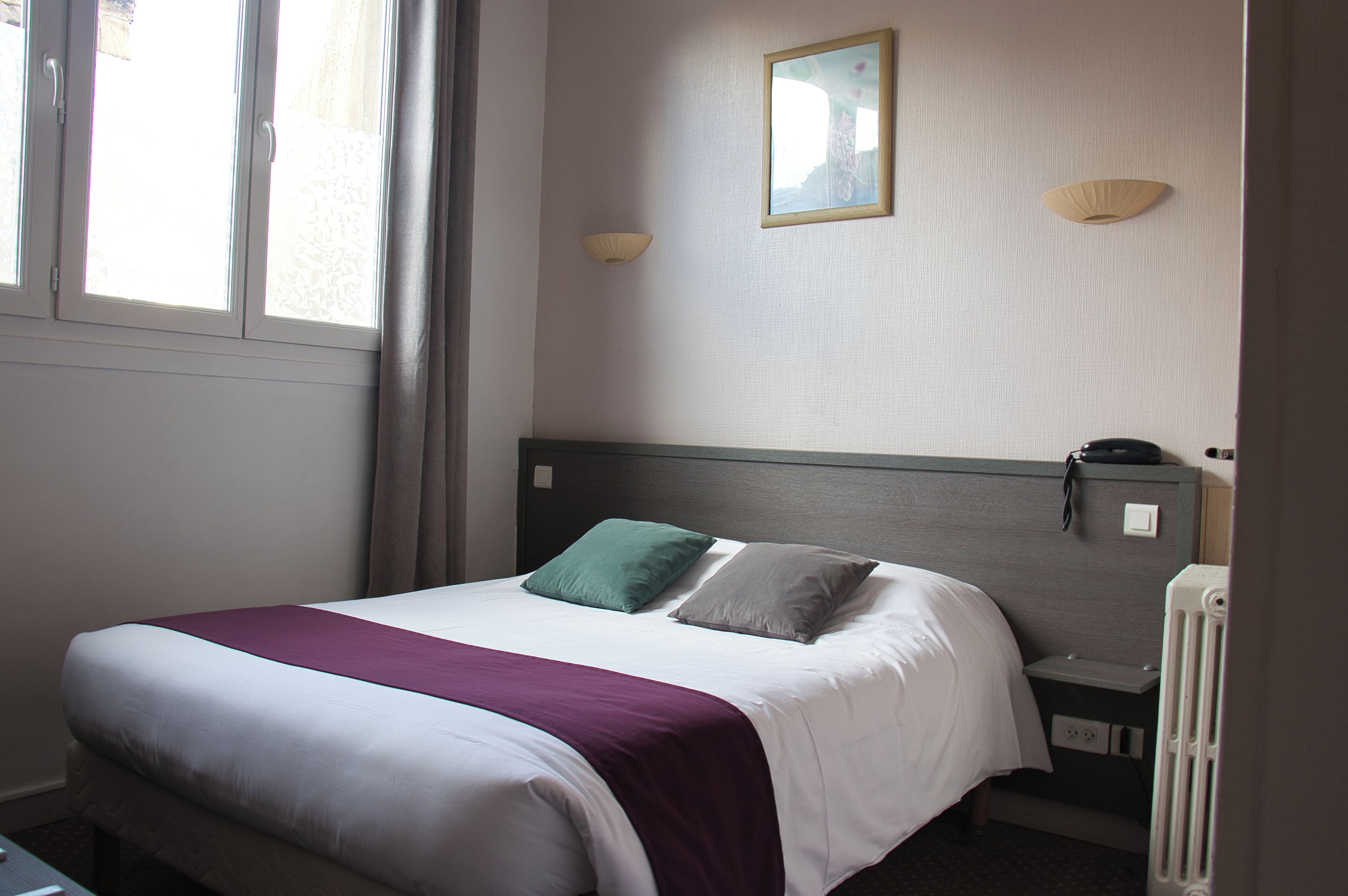 A hotel room with a bed, a nightstand, a lamp, and a window with curtains.