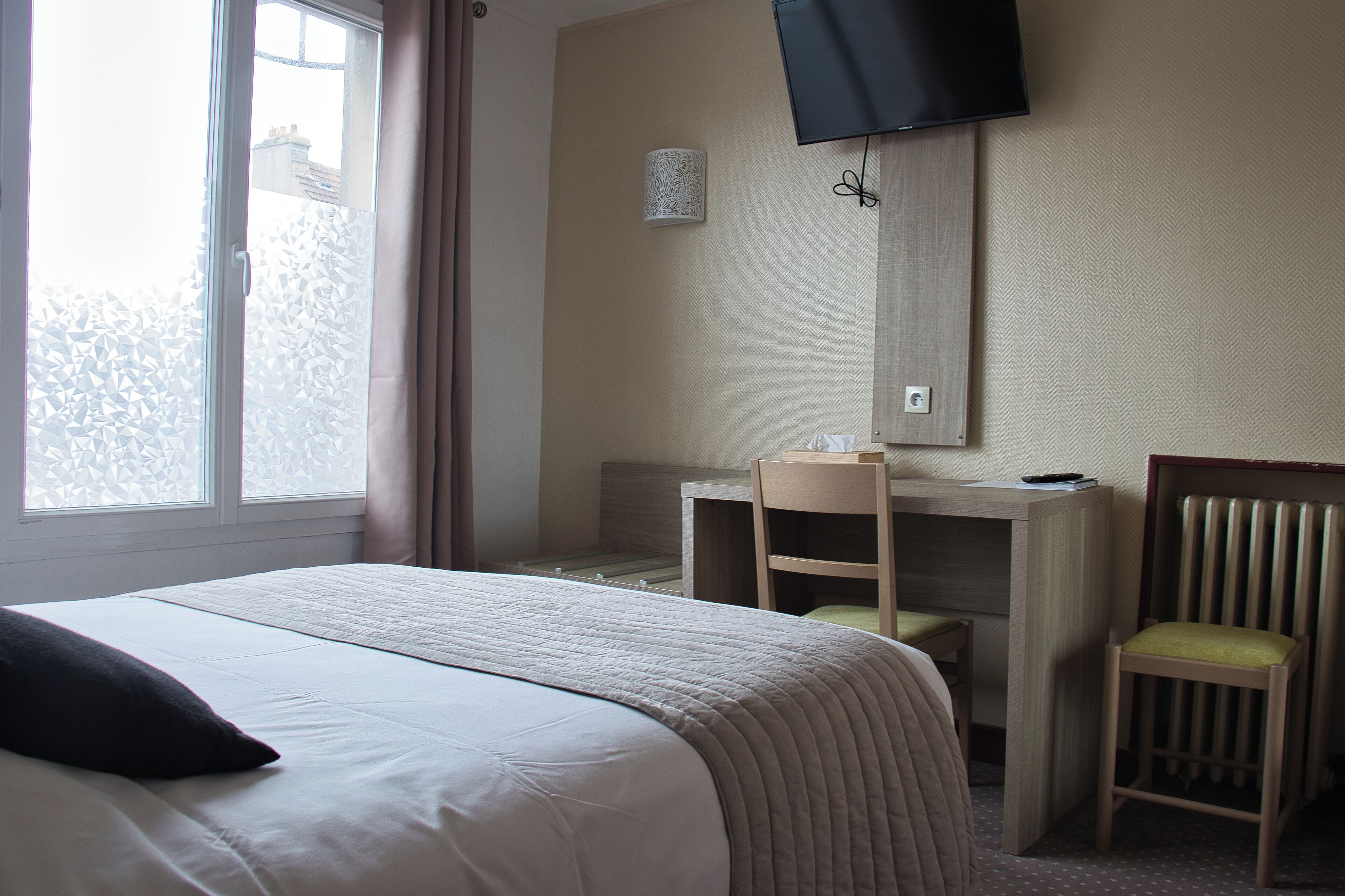 Una habitación de hotel con cama, escritorio, silla, televisión y ventana con cortinas.