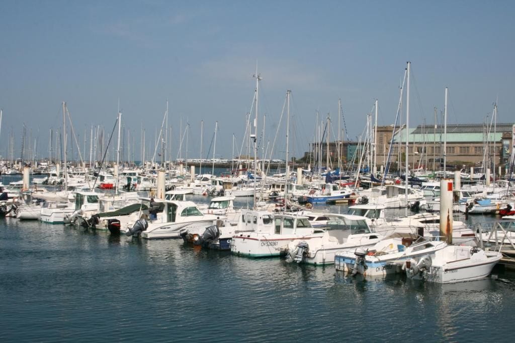 Un port de plaisance où sont amarrés de nombreux bateaux, un bâtiment en arrière-plan et une eau calme.