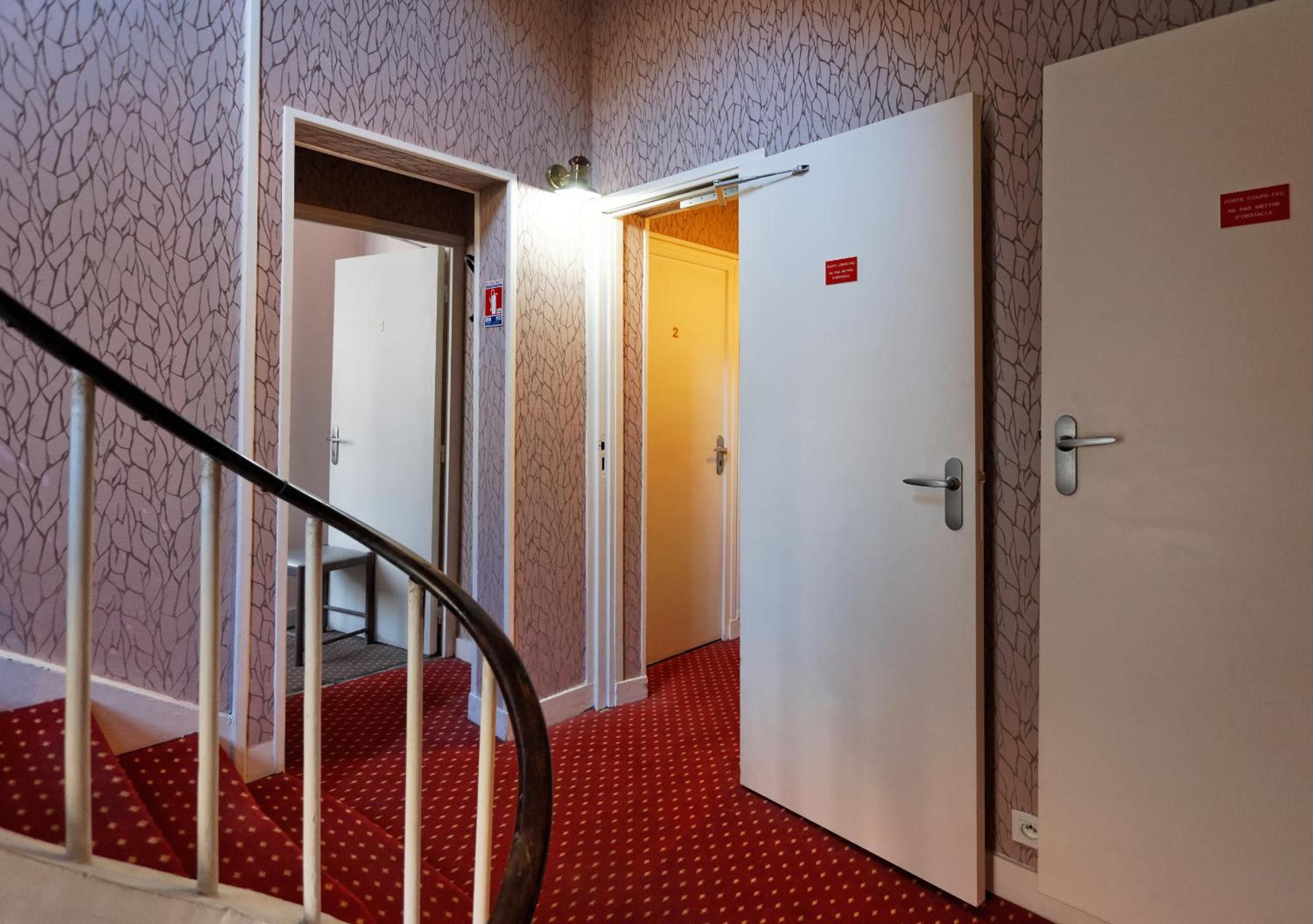 Pasillo de hotel con una escalera, una puerta numerada y un letrero que indica una salida de emergencia.