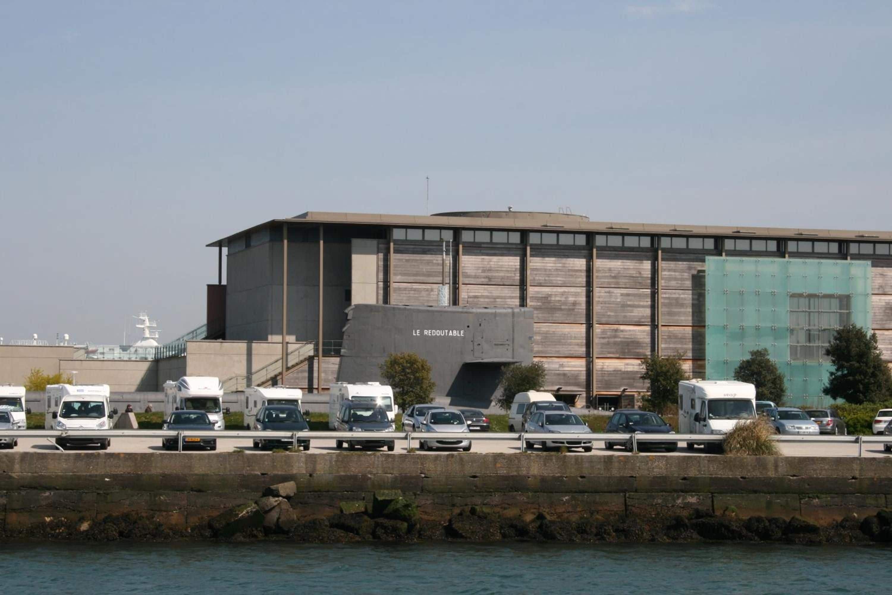 A building with a large parking area in front, a body of water, and a clear sky.