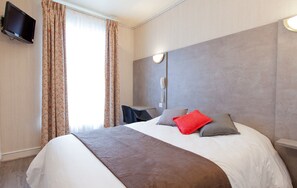A hotel room with a large bed, a flat-screen TV mounted on the wall, a desk with a chair, and a window with curtains. - Panam Hotel (Paris)
