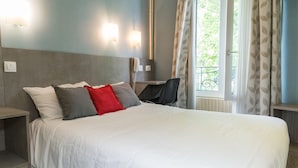 A hotel room with a large bed, a desk, and a chair. There are two wall-mounted lights and a window with curtains. - Panam Hotel (Paris)