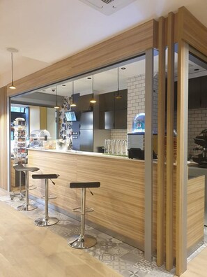A modern bar area with wooden accents, bar stools, and a visible kitchen in the background. - Panam Hotel (Paris)