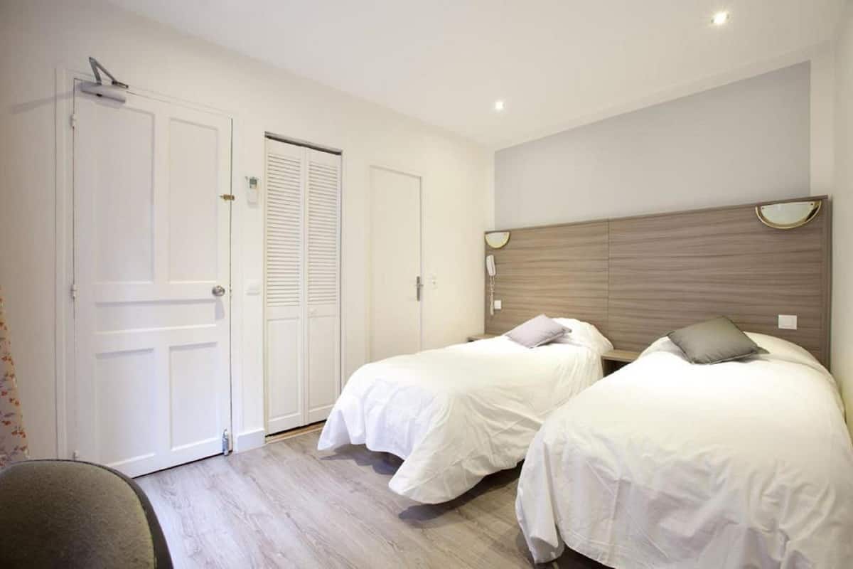 A bedroom with two beds, a wooden headboard, a bedside table with a lamp, and a door with a window.
