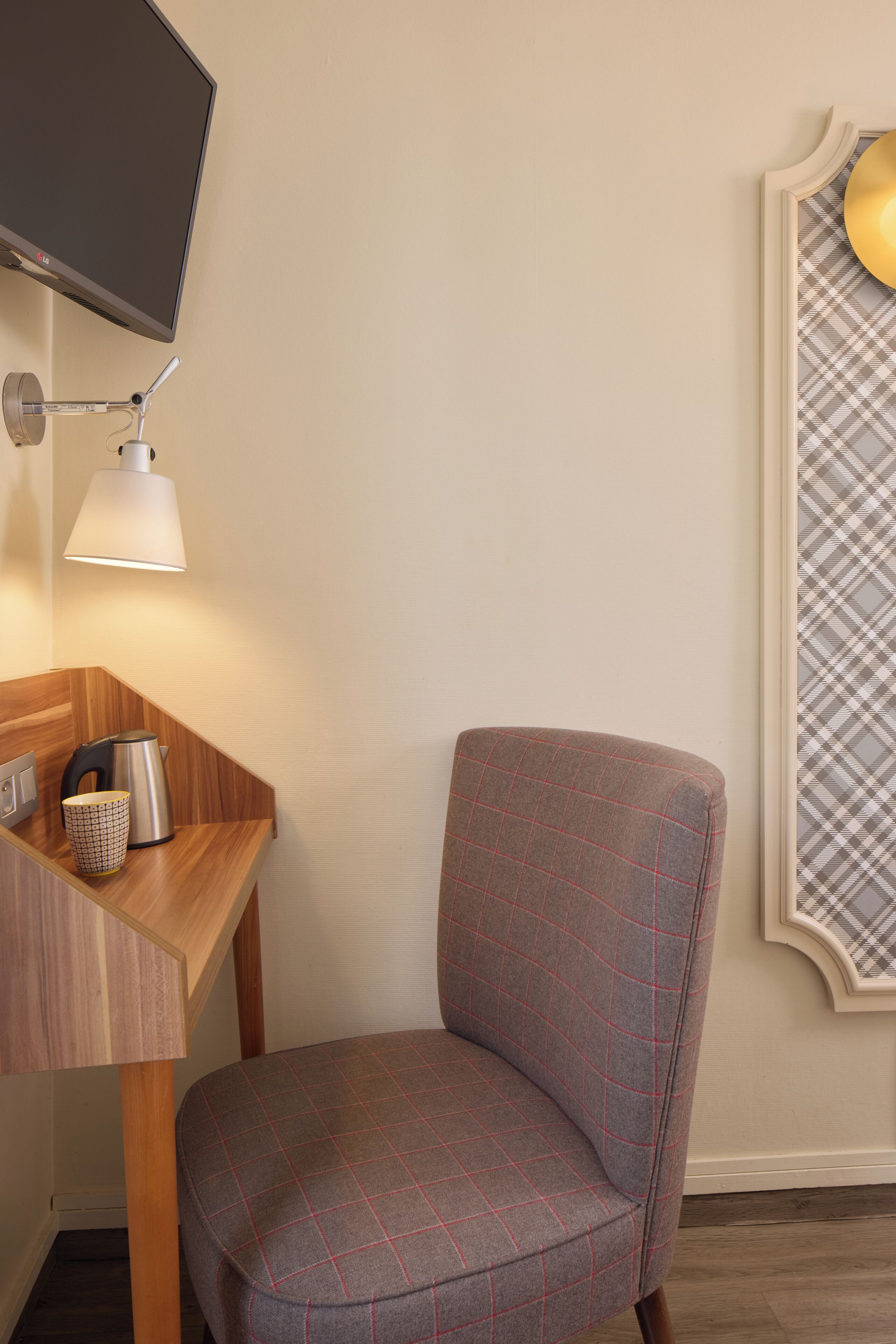 Een kamer met een wandtelevisie, een bureau met een lamp, een stoel en een decoratieve wandversiering met een patroon.