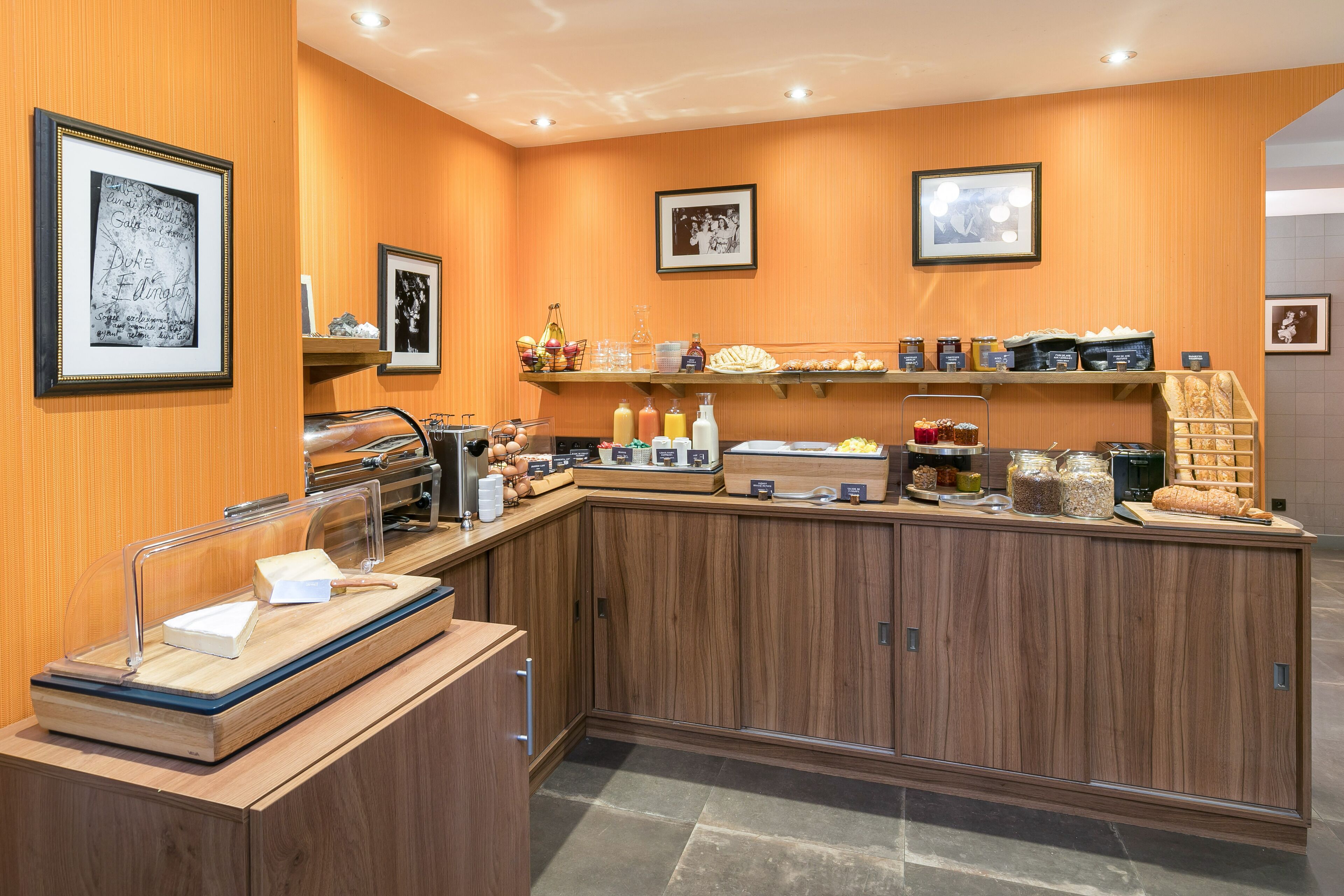 A breakfast bar with various food items and condiments, framed pictures on the walls, and a wooden counter.