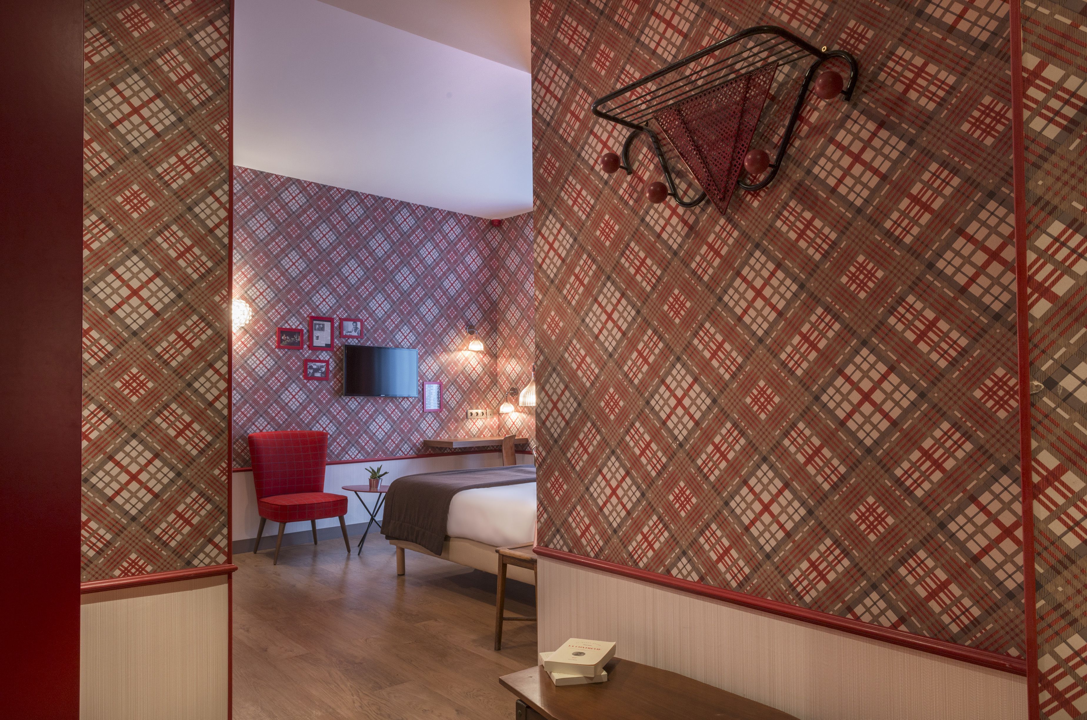 Une chambre d’hôtel avec un papier peint à motifs, une chaise rouge, un lit, une table de chevet et un téléviseur fixé au mur.
